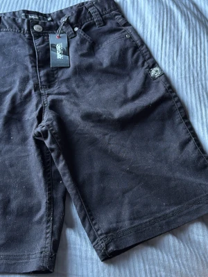 Svarta shorts från ZXR med fickor - Snygga svarta shorts från ZXR med klassisk femficksdesign och knappgylf. Shortsen har en rak passform och är tillverkade i ett mjukt bomullsmaterial. Perfekta för varma dagar och enkla att matcha med olika stilar.