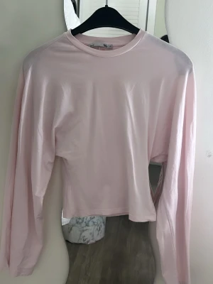 Ljusrosa långärmad topp från H&M - En enkel och stilren ljusrosa långärmad topp från H&M. Toppen har rund halsringning och är gjord i ett mjukt material som känns skönt mot huden. Perfekt att matcha med jeans eller kjol för en clean look.