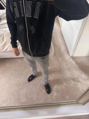 Svart zip hoodie från Amici - Säljer en svart hoodie med dragkedja från Amici. Hoodien har vita broderade detaljer och texten 'AMICI' på bröstet samt två fickor framtill. Utrustad med huva och tillverkad i mjukt sweatshirtmaterial. Perfekt för en chill och avslappnad stil.