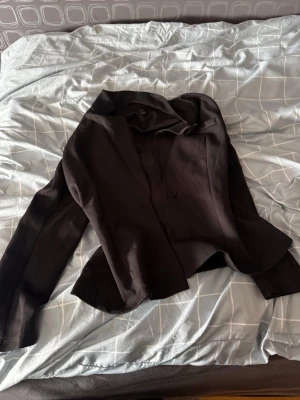 Svart kavaj från H&M - Stilren svart kavaj från H&M med enkelknäppning och klassisk krage. Modellen har en rak passform och långa ärmar. Perfekt för dig som vill ha en tidlös och enkel look. Materialet känns mjukt och följsamt.