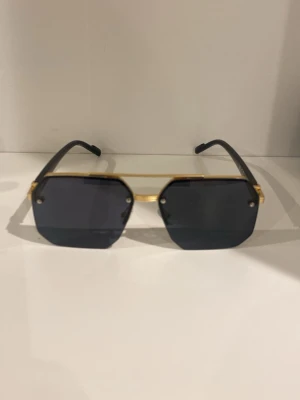 Svarta fyrkantiga solglasögon guld - Snygga solglasögon med fyrkantiga svarta glas och guldfärgade detaljer. Bågarna är svarta och glasen är mörka, vilket ger en cool och modern look. Perfekta för att lyfta din stil under soliga dagar.