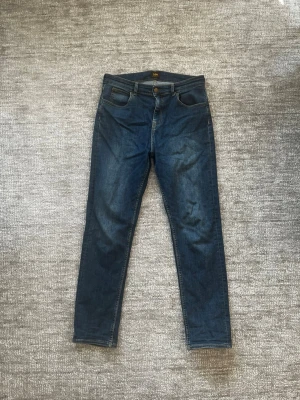 Mörkblå slim fit jeans från Lee - Snygga mörkblå skinny jeans från Lee med klassisk femficksdesign och Lee-logga på bakfickan. Jeansen har en smal passform och är tillverkade i stretchigt denimtyg för extra komfort. Perfekta för en trendig och avslappnad stil. Passar allt mellan 170-180cm