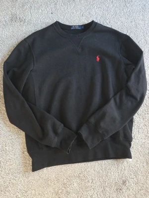 Svart Polo tröja - Klassisk svart sweatshirt från Polo Ralph Lauren med röd broderad logga på bröstet. Tröjan har rund halsringning, långa ärmar och ribbade muddar. Tveka inte på att ställa frågor eller diskutera priset.🙌🏼✨️
