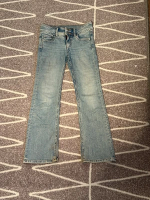 Ljusblå bootcut jeans - Säljer ett par ljusblå bootcut jeans med klassisk femficksdesign och dragkedjegylf. Jeansen har en lätt tvättad look och raka ben som går ut lite nedtill. Perfekta för en avslappnad och trendig stil. Bra skick