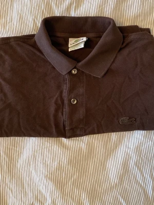 Brun Lacoste piké  - Storlek S, mycket bra skick, lite skrinklig på bild men det är ingen defekt. Pris kan diskuteras.