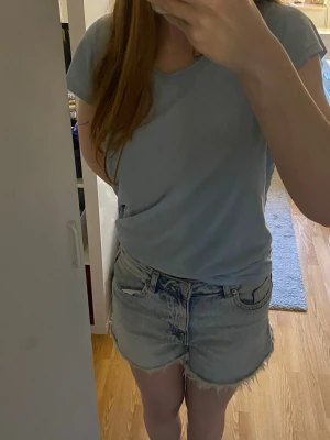 Ljusblå jeansshorts med fransig kant - Snygga ljusblå jeansshorts med fransig kant nertill och klassisk femficksdesign. Shortsen har hög midja och har en gylf med dragkedja, ej knappar. Jag har använt max 3 gånger. Perfekta för varma dagar och enkla att matcha med olika toppar.