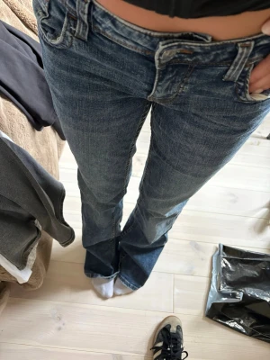 Blå bootcut jeans med slitningar bak - Säljer ett par blå bootcut jeans med snygga slitningar och klassisk femficksmodell. Jeansen har låg midja och är tillverkade i ett robust denimtyg. Perfekta för en avslappnad och trendig look.