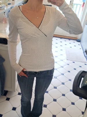 svartvit polka dot omlottopp - snygg vit omlottopp med svarta prickar och svarta kanter vid v-ringningen 💕 långärmad med figurnära passform. säljer pga att jag inte gillar materialet (95% polyester) i nyskick! aldrig använd💕