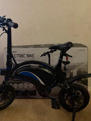 Svart elcykel Andersson E-Bike 5000 - Säljer en svart elcykel Andersson E-Bike 5000 med blå och vita detaljer. Cykeln har en kompakt och vikbar design, 12-tums hjul, skivbromsar och batteri som räcker långt. Perfekt för dig som vill ha en smidig och elektrisk cykel för stan.