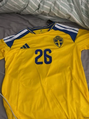 Sverige tröja Strlk M - Gul svensk landslagströja från Adidas med blå detaljer, nummer 26 och texten 'GRÄVA GULD' på ryggen. Tröjan var för stor för mig därav säljer jag den för att köpa i mindre storlek!