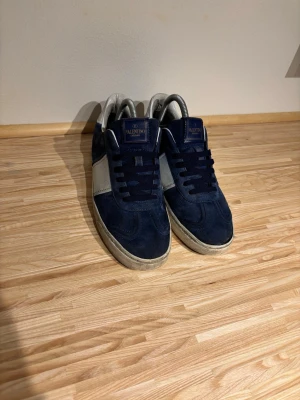 Valentino flycrew  - Snygga sneakers från Valentino i mörkblå mocka och vitt läder. Skorna saknar 5 nitar totalt. Två på vänster och tre på höger. Snörerna är inte original.