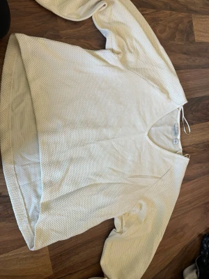 Vit strukturerad tröja från b.young - Snygg vit långärmad tröja från b.young med v-ringning och diskret strukturmönster i tyget. Perfekt för en clean och stilren look. Tröjan har en avslappnad passform och är lätt att matcha med olika outfits, använd 1 gång. 