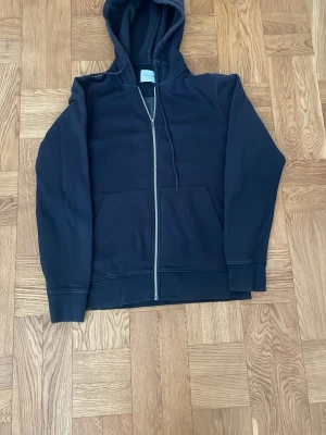 Svart zip-hoodie med huva XS - En svart hoodie med dragkedja och huva. Modellen har två stora fickor framtill och justerbara snören i huvan. Använd men bra skick.