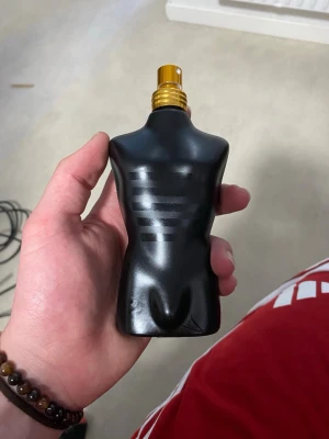 Jean Paul Gaultier Le Male Parfym - Säljer en Jean Paul Gaultier Le Male parfym i en cool svart flaska formad som en manlig torso. Flaskan har mattsvart finish med subtila ränder på framsidan och guldfärgad spraytopp. Perfekt för dig som gillar unika och snygga parfymflaskor.