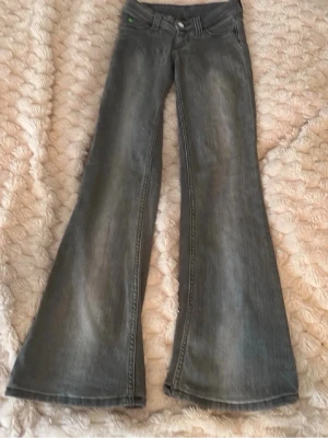 Gråa bootcut jeans med utsvängda ben - Säljer ett par gråa bootcut jeans med riktigt utsvängda ben. Klassisk femficksmodell och låg midja. Jeansen har en snygg tvättad look och är tillverkade i denim. Perfekta för dig som gillar retrostil och vill sticka ut.