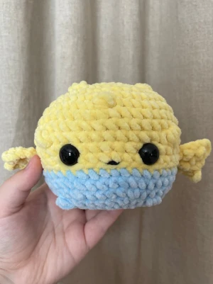 Handvirkad fisk i chenille – ca 11 cm - Handvirkad fisk i mjukt chenillegarn i gula och ljusblå toner med små fenor och stora säkerhetsögon. En söt och kompakt liten plushie som passar perfekt som present eller som gullig detalj i hemmet. Varje exemplar är unikt och gjort helt för hand. Ca 11 cm hög.