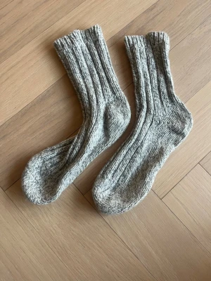 Grå stickade ullstrumpor - Mysiga grå stickade strumpor i ull med ribbad struktur. Perfekta för kalla dagar och ger en klassisk look. Tjockt och värmande material som passar bra till både hemmamys och utomhusaktiviteter.