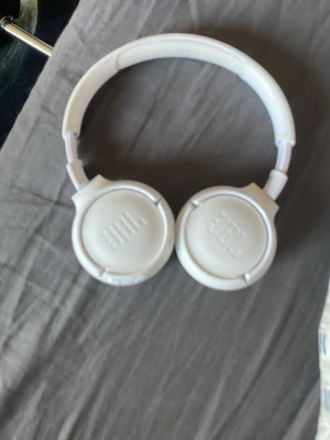 Vita JBL over-ear hörlurar - Säljer ett par stilrena vita over-ear hörlurar från JBL. De har en rund form med mjuka, vadderade kåpor och justerbart huvudband. Perfekta för att lyssna på musik eller poddar med skön komfort och snygg design.