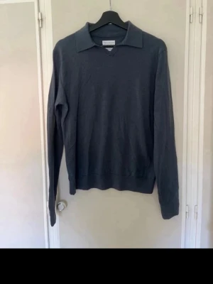 Blå tröja med krage - Snygg stickad pikétröja i blå från These Glory Days, tillverkad i mjuk superior merinoull. Tröjan har klassisk krage och v-ringning, perfekt för en stilren och avslappnad look.