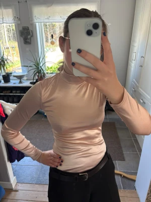 Ljusrosa body med lång ärm - Snygg ljusrosa bodysuit med lång ärm och polokrage. Materialet är glansigt och stretchig. Knappt använd och inga synliga tecken på slitage.