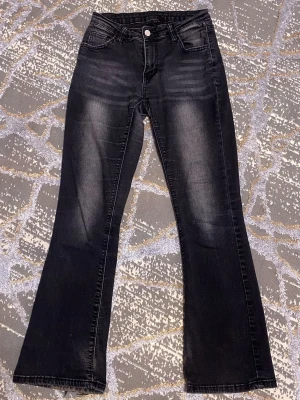 Svarta bootcut jeans  - Snygga svarta bootcut jeans med diskreta slitningar framtill och klassiska fem fickor. Jeansen har en lätt utsvängd passform nertill och stängs med knapp och dragkedja. Perfekta för en trendig och avslappnad look.