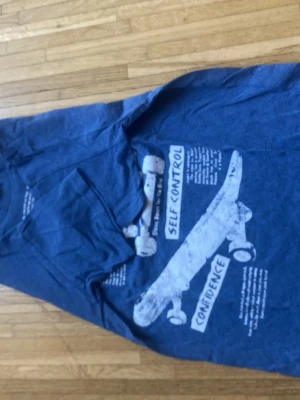 Blå t-shirt med skateboardtryck - Blå t-shirt med coolt skateboardtryck och texten 'Self Control' och 'Confidence' på framsidan. T-shirten har rund hals och korta ärmar, perfekt för en avslappnad streetstil. Materialet känns mjukt och bekvämt, troligen bomull eller bomullsblandning.