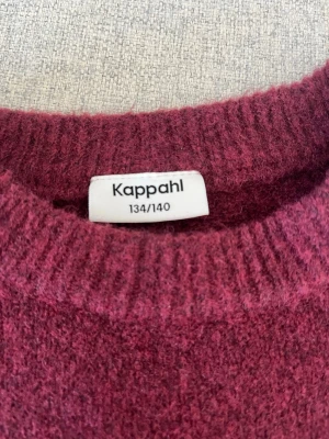 Vinröd stickad tröja från Kappahl - Mysig vinröd stickad tröja från Kappahl med puffärmar och rund hals. Tröjan har ribbstickade muddar vid hals, ärmslut och nederkant. Perfekt för dig som gillar en enkel men ändå trendig look.för barn 