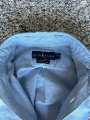Ljusblå skjorta från Ralph Lauren XS - Snygg ljusblå skjorta från Ralph Lauren i slim fit-modell. Skjortan har klassisk krage, långa ärmar och knappar framtill. Tillverkad i bomull med stretch för extra komfort. Ikoniska loggan broderad på bröstet.