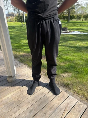 Svarta mjukisbyxor  - Svarta mjukisbyxor med resår i midjan och  perfekt passform. Byxorna har muddar vid bensluten och en avslappnad, rak passform. Perfekta för chill eller träning. Liten vit logga på sidan av midjan. Mjukt och bekvämt material.