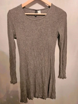 Klänning tunika H&M divided 40 - Grå klänning tunika från H&M divided 40  Säljer en grå ribbad klänning från H&M i storlek 40. Klänningen har långärmade ärmar och en rund halsringning. Den är kort i modellen och har vågiga kanter vid ärmslut och nederkant för en extra detalj. Perfekt för dig som gillar enkel och stilren design.  Kan även hämtas I Partille  E1