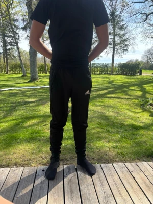 Svarta Adidas herr - Svarta mjukisbyxor från Adidas med smal passform och klassisk logga på vänster lår. Byxorna har resår i midjan och vid benslut, samt sidofickor. Perfekta för chill eller träning. Små i storlek