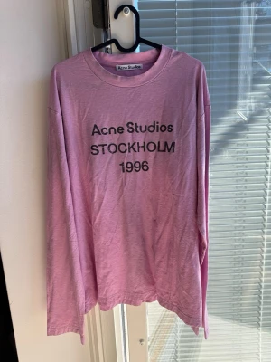 Långärmad rosa t-shirt Acne Studios - Långärmad rosa t-shirt från Acne Studios med tryck 'STOCKHOLM 1996' på bröstet. Klassisk rund hals och avslappnad passform. Perfekt för dig som gillar stilrena och trendiga plagg med statement-tryck.
