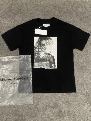 Maison Margiela svart t-shirt med print - Svart t-shirt från Maison Margiela med coolt grafiskt print framtill i vitt och grått. Klassisk passform med rund hals och korta ärmar. Perfekt för dig som gillar streetstyle och designerplagg.