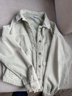 Ljusgrön jeansjacka från Zara - Trendig ljusgrön jeansjacka från Zara med klassisk krage, knappstängning framtill och två bröstfickor. Jackan har en avslappnad passform och är tillverkad i ett mjukt denimtyg. Perfekt för dig som vill ha en stilren och enkel look.