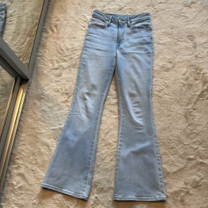 Ljusblå bootcut jeans med hög midja - Säljer ett par ljusblå bootcut jeans med hög midja och klassiska fem fickor. Jeansen har utsvängda ben och är tillverkade i ett mjukt denimtyg. Perfekta för en trendig och avslappnad look.