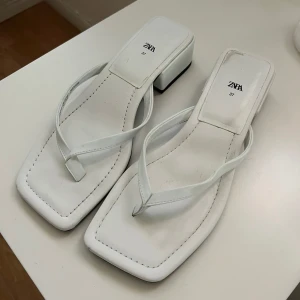 Vita sandaler med klack från Zara - Stilrena vita sandaler från Zara med fyrkantig tå och låg blockklack. Remmarna är tunna och i samma vita färg som sulan. Perfekta för en trendig look och lätta att matcha med olika outfits.