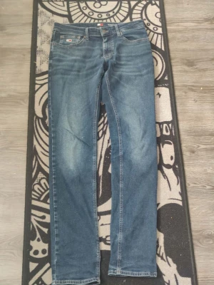 Blå raka jeans från Tommy Hilfiger - Snygga blå jeans från Tommy Hilfiger med klassisk femficksdesign och raka ben. Jeansen har diskreta slitningar framtill och bakfickor med logodetalj. Perfekta för en avslappnad och stilren look.