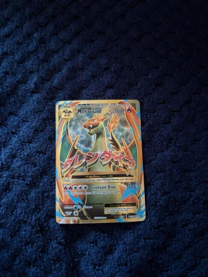Pokémonkort Mega Charizard EX - Säljer ett samlarkort från Pokémon, Mega Charizard EX med 220 HP. Kortet har färgstark design med orange, blå och gul bakgrund samt japansk text. Perfekt för dig som gillar att samla eller spela Pokémonkort.