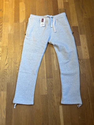 Ljusgrå mjukisbyxor  - Säljer ett par ljusgrå mjukisbyxor från RusseMerch. Dragkedja vid fickorna och snörning vid benslut. Aldrig använda och prislappen kvar. Hör av dig vid fråga eller fundering!