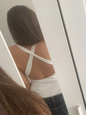 Vit body med korsade axelband - Säljer en stilren vit body med korsade axelband i ryggen. Bodyn har en enkel, tight passform och är tillverkad i ett mjukt, stretchigt material som sitter bekvämt mot kroppen. Perfekt att matcha med jeans eller kjol för en clean look.