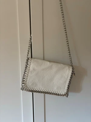 Vit axelväska med kedjerem - Vit axelväska med silverfärgad kedjerem och detaljer runt kanterna. Aldrig använd. 
