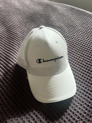Vit keps från Champion - Snygg vit keps från Champion. Använd någon gång förra sommaren men blev bara  liggandes i en låda. Liten mörk fläck på framsidan, inte testat att få bort. 