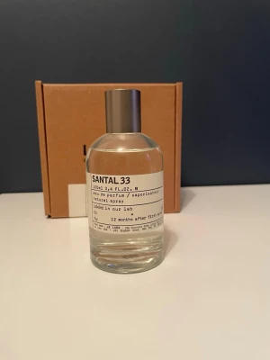 Le Labo Santal 33 Eau de Parfum 100ml - Le Labo Santal 33 är en ikonisk parfym i en minimalistisk, genomskinlig glasflaska med metallock. Doften är känd för sina träiga och kryddiga toner, och flaskan rymmer 100 ml. Etiketten har en stilren, laboratorieinspirerad design. Använd endast några få ml