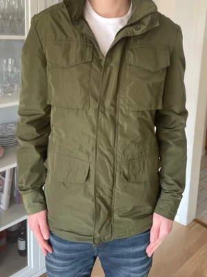 Grön Fieldjacka från Bläck - S - Jag säljer den här riktigt snygga fieldjackan från bläck i storlek S. Den är i fint skick och är ett perfekt plagg nu inför vår och sommar. Nypris låg på ca 2299kr och jag säljer den här för 799kr. Tveka inte att höra av er!