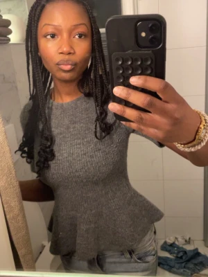 Grå stickad plepumtopp  - Säljer en grå ribbad peplumtop från h&m med korta ärmar och rund hals. Toppen har en snygg volangdetalj nedtill och är jätte mysig att ha på sig💓