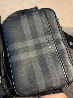 Burberry axelväska - Burberry Check Messenger Bag.                                       Köpt från Miinto för 10 500 kr, kvitto finns. Väskan är i fint skick, se bilder. Mindre slitage vid axelremmens fäste har tidigare funnits, men detta är professionellt åtgärdat hos läderreparatör. Väskan har många år kvar att bäras vidare. 