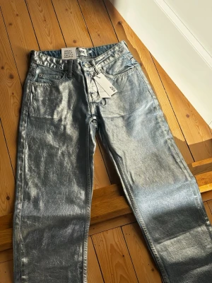 Silvriga raka jeans med metallic finish - Nya med prislapp kvar. Nypris 400:-     Säljer ett par riktigt snygga jeans i metallic silver med rak passform och klassisk femficksdesign. Byxorna har normal midja och är tillverkade i ett glansigt material som verkligen sticker ut. Perfekta för dig som vill ha något unikt och vågat i garderoben.