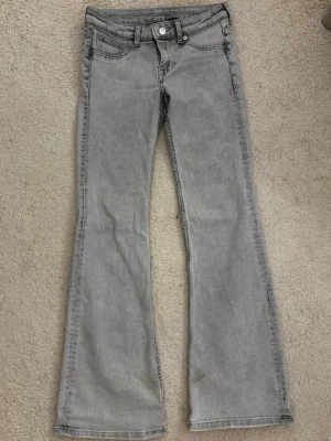 Grå bootcut jeans med låg midja från H&M - Snygga grå jeans med bootcut-modell och låg midja. Klassisk femficksdesign och knappgylf. Jeansen har en lätt tvättad look och är tillverkade i mjukt denimtyg som ger en avslappnad vibe.(Säljs inte längre)
