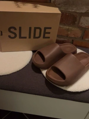 Bruna Yeezy Slide tofflor från Adidas - Yeezy slides i gott skick, storlek 10 44,5 så passar allt från 42-44,5. BVSA