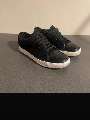 Svarta sneakers med vit sula - Snygga svarta sneakers med vit sula och klassisk låg profil. Skorna har svarta skosnören och ovandel i blankt material som ger en stilren look. Perfekta för dig som gillar enkel och clean stil. Whitning 